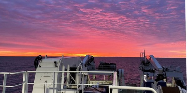 Utsikt fra akterenden på et skip og bakover mot en fargerik soloppgang.