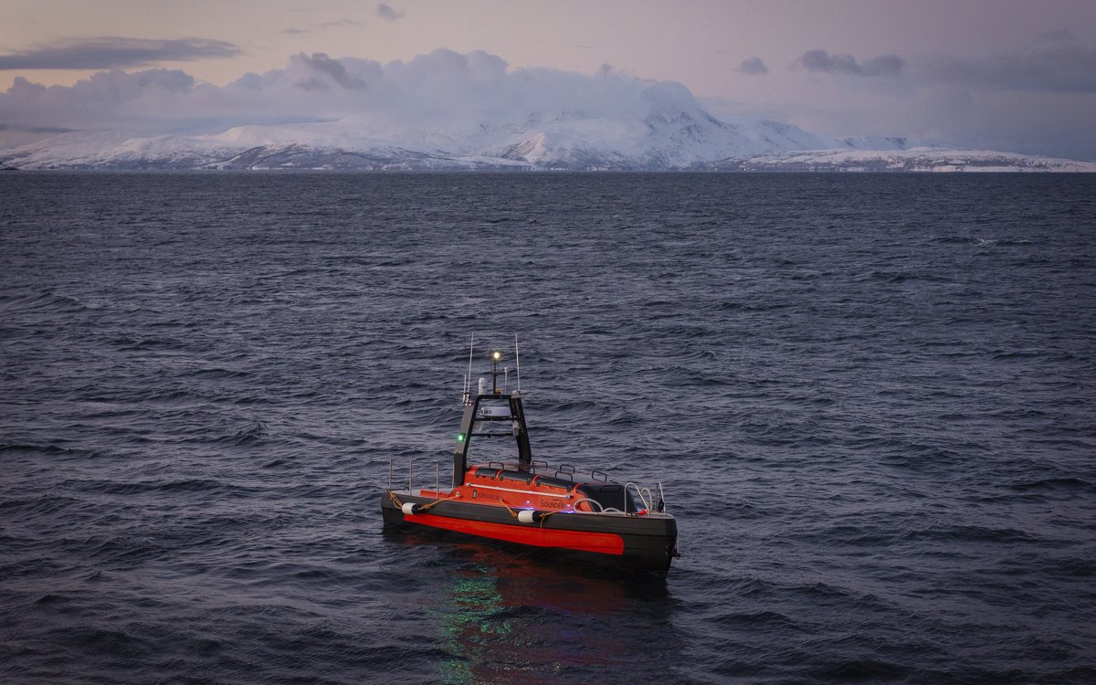 Kongsberg Discovery Sounder USV (ubemanna overflatefartøy) med navnet Frigg ute på havet. Snødekte fjell i bakgrunnen.