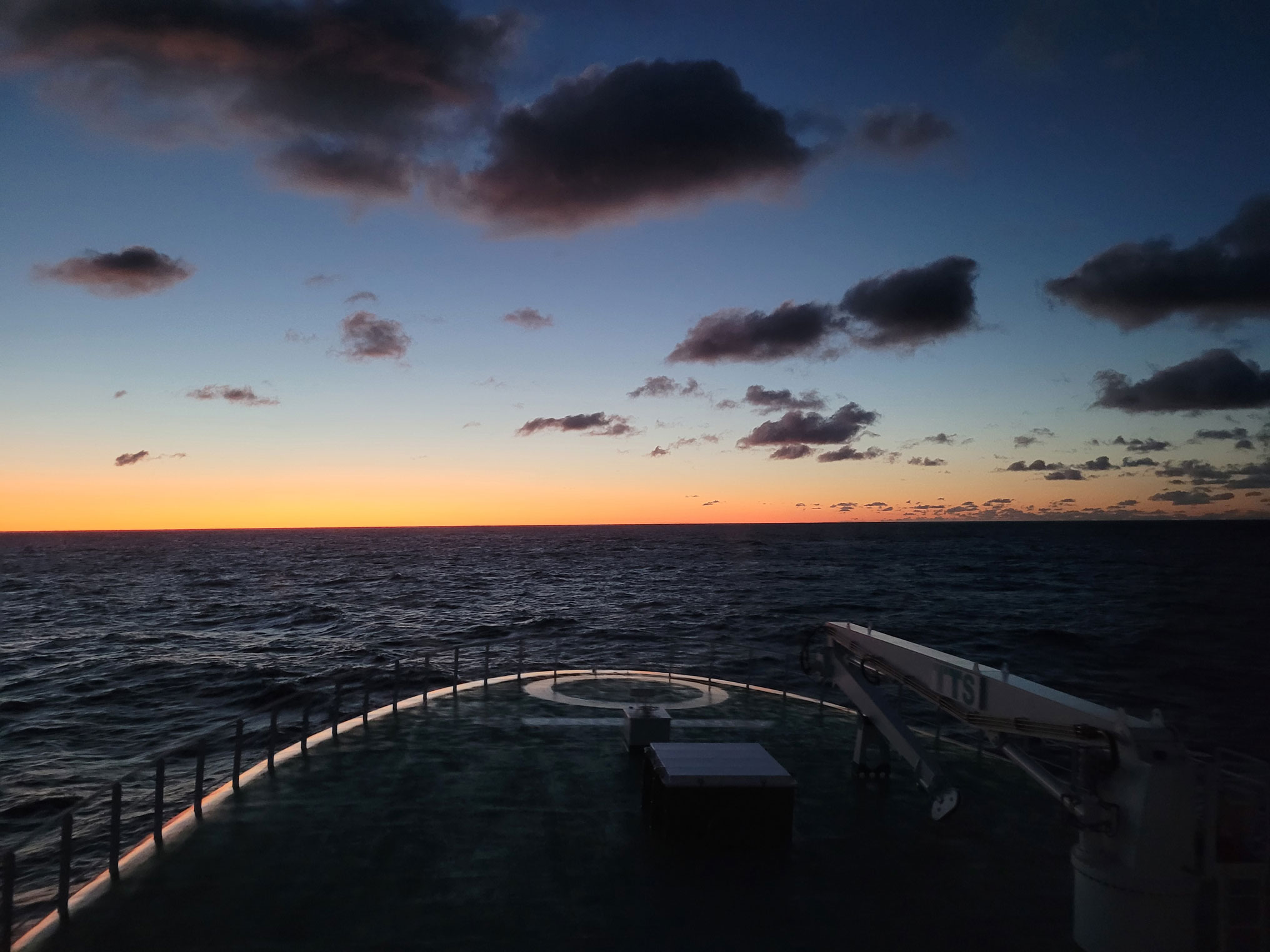 Utsikt fram over bauen, rolig sjø og solnedgang. Spredte skyer.