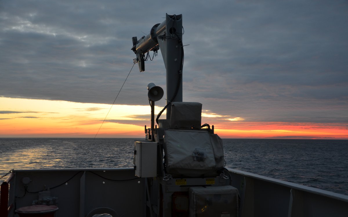 Utsikt fra om bord et større fartøy ut mot havet med skyer og rød himmel i horisonten.