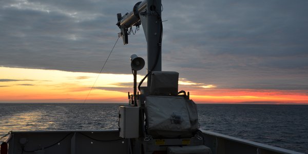 Utsikt fra om bord et større fartøy ut mot havet med skyer og rød himmel i horisonten.
