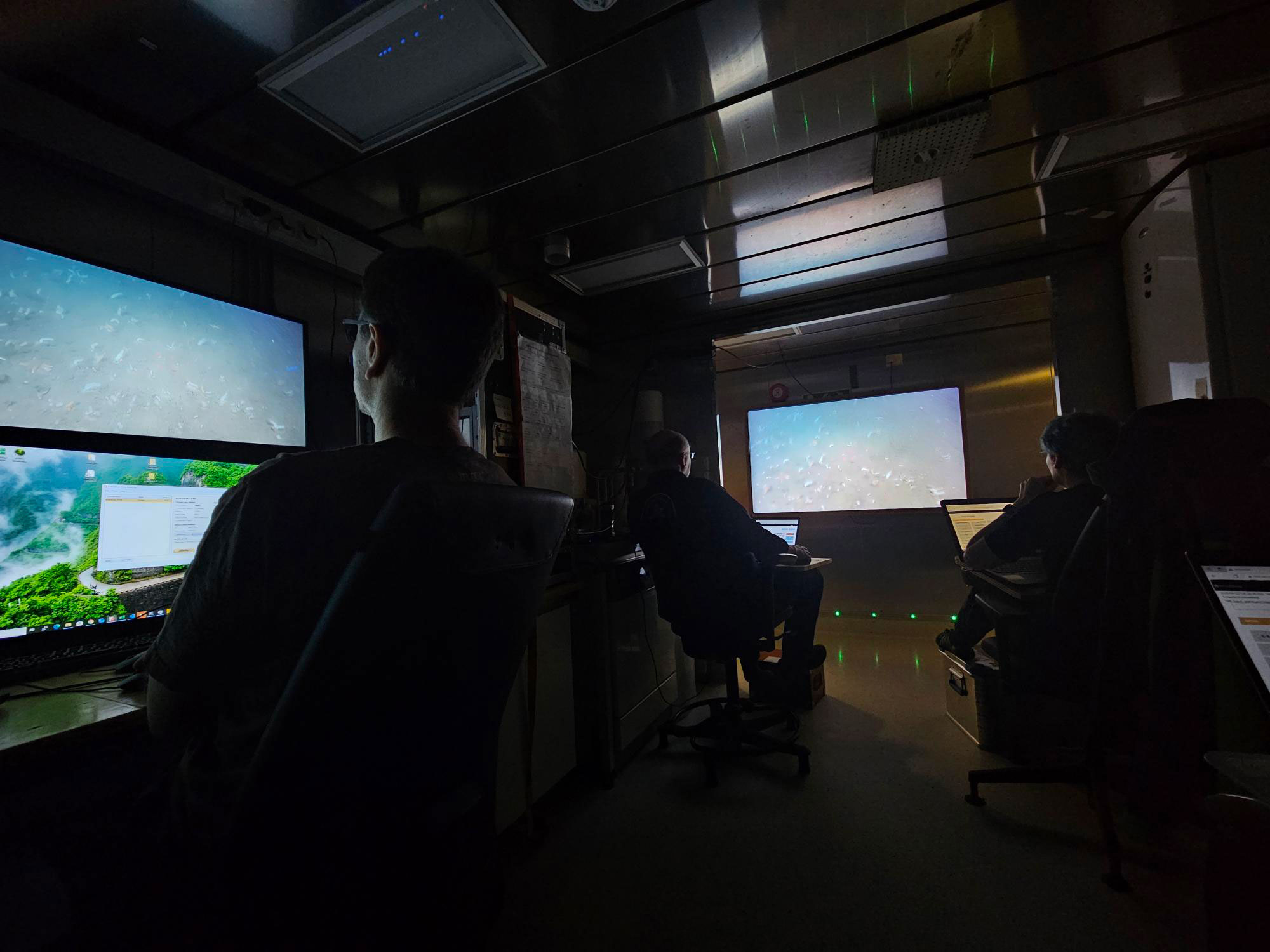 Tre personer sitter i et mørkt rom og følger med på flere ulike skjermer. De har pc'er der de skriver ned observasjoner.